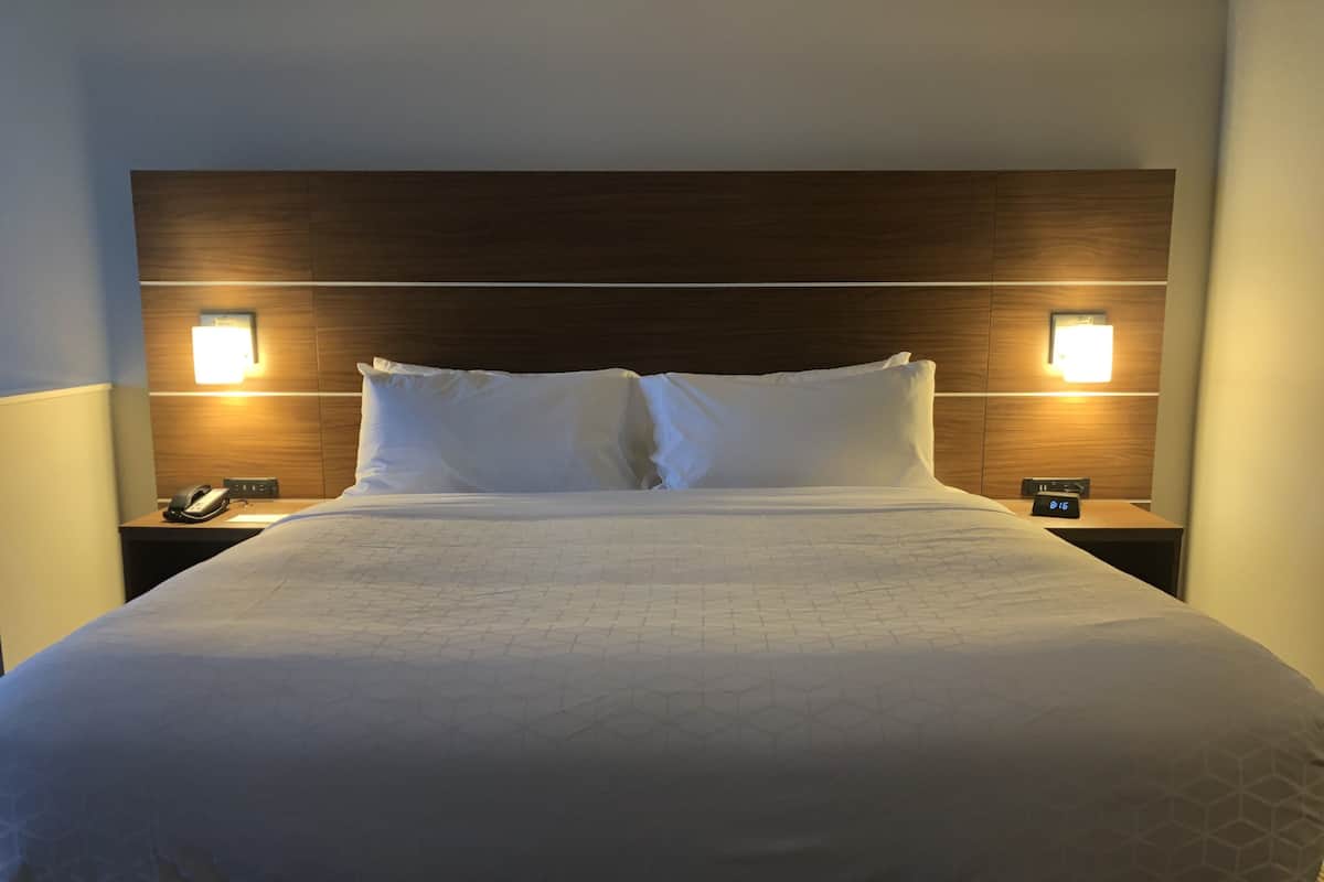 A hotel room with a large bed, two bedside tables, a nightstand, and a wall-mounted clock.