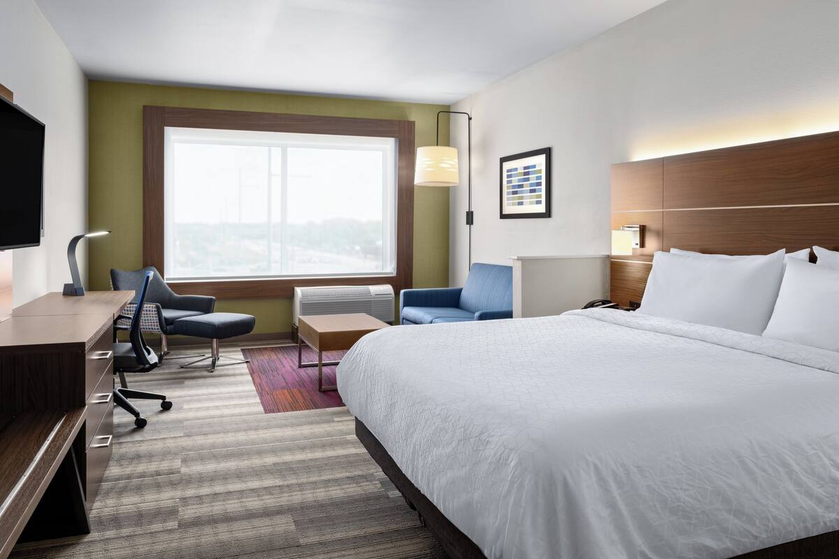 A hotel room with a large bed, a desk with a chair, a TV, and a window with a view.