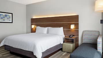 A hotel room with a large bed, bedside tables, a nightstand, a chair, and a small ottoman.