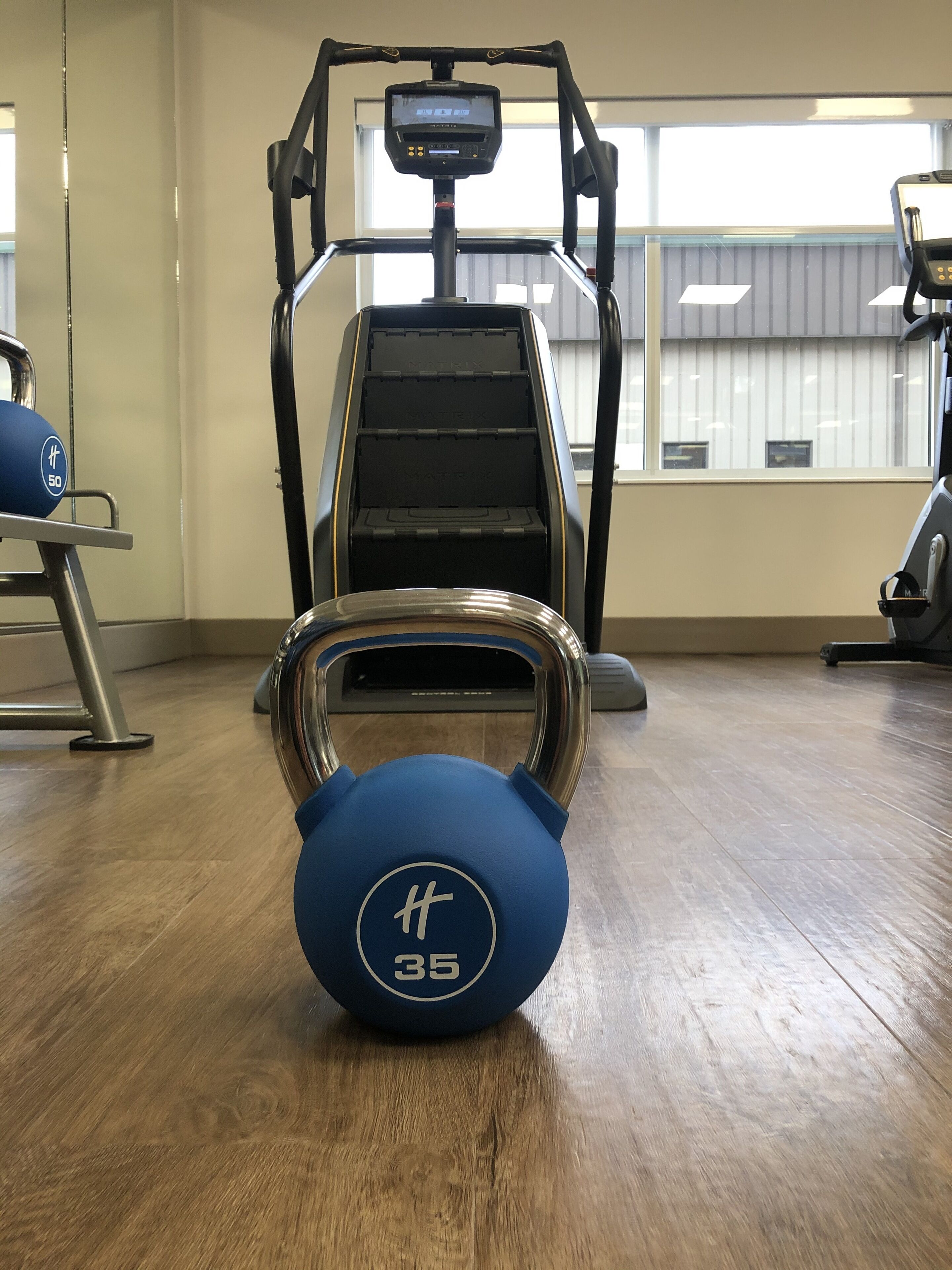 A gym with a blue kettlebell, a treadmill, and a rowing machine.