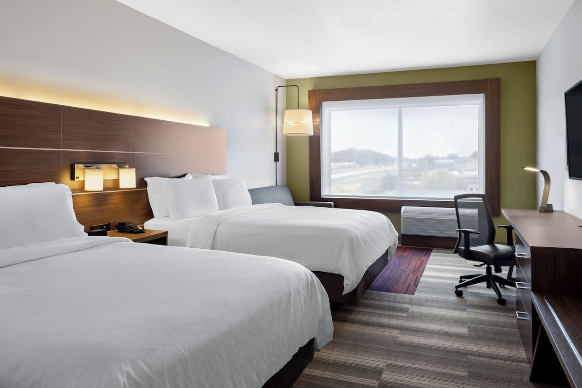 A hotel room with two beds, a desk, a chair, a TV, and a large window with a view.