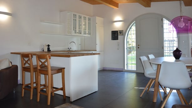 A modern kitchen with white cabinets, a wooden island, and a dining area with white chairs and a table.