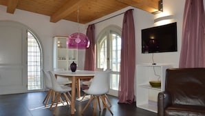A dining area with a round table, white chairs, and a purple pendant light. There is a brown leather chair in the foreground.