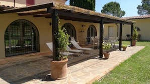 A covered patio with stone flooring, outdoor seating, and potted plants.