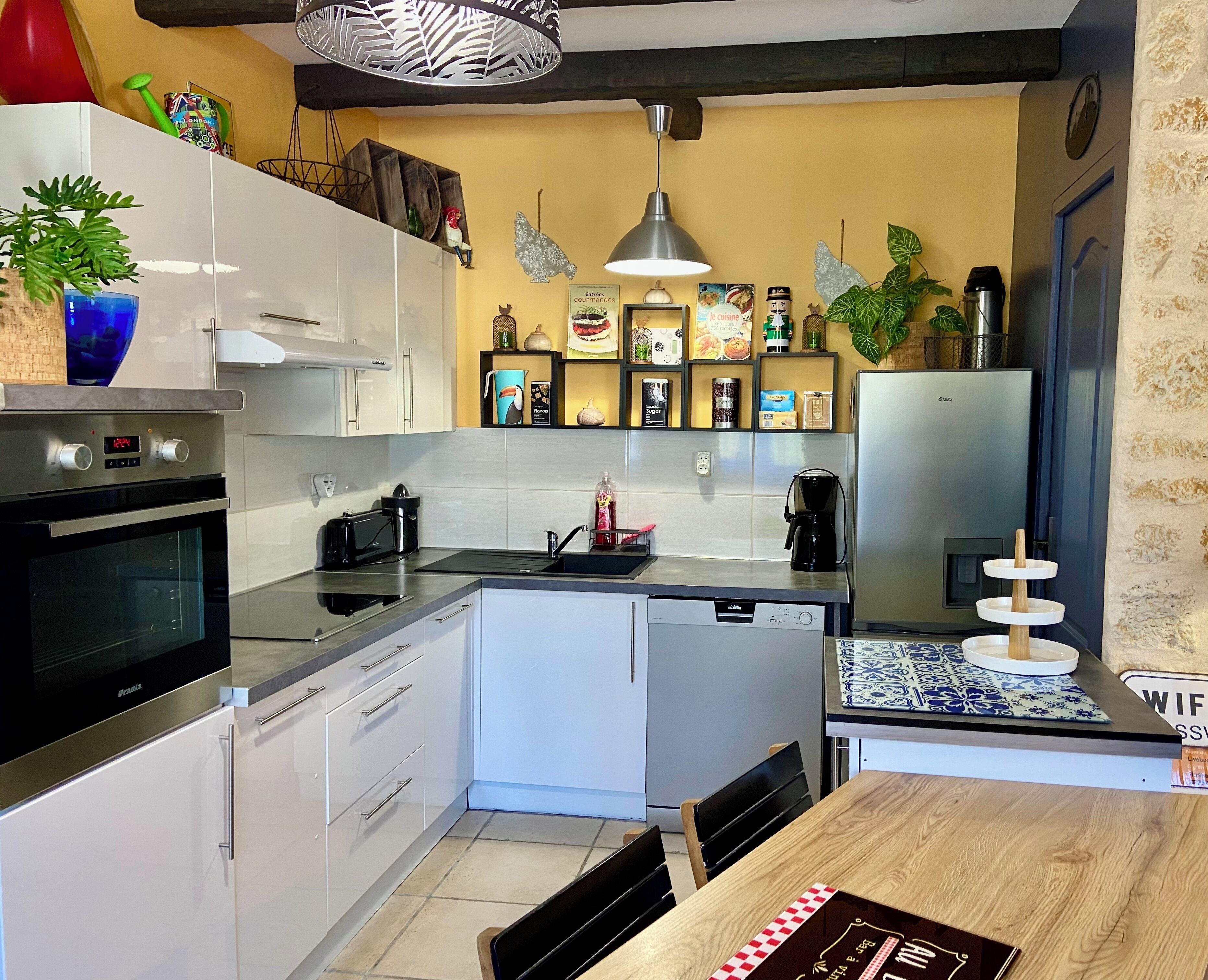 Una cocina moderna con armarios blancos, un refrigerador de acero inoxidable, horno empotrado y cafetera.