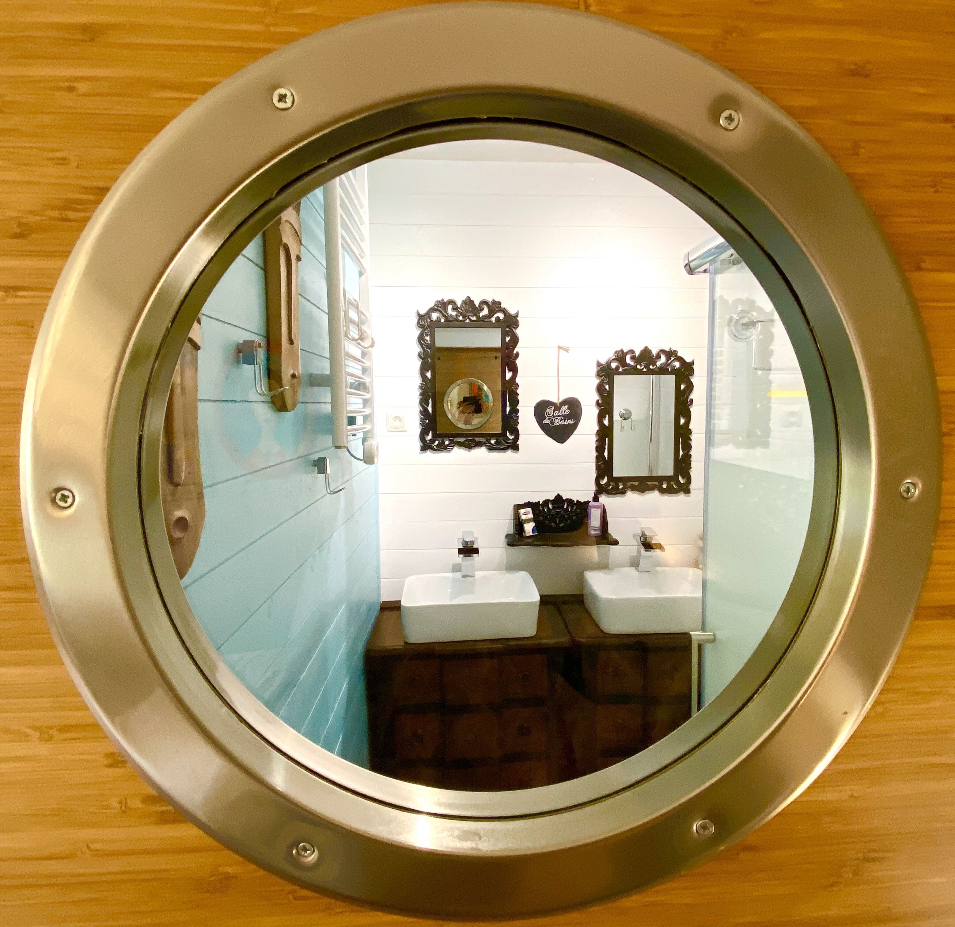A bathroom with a round mirror, two sinks, a vanity, and a decorative mirror with a heart-shaped sign.