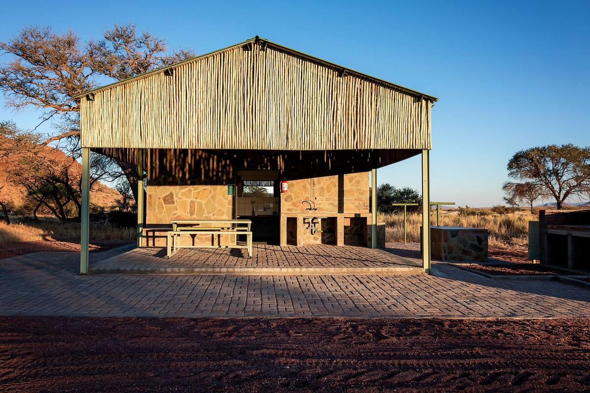 A rustic wooden structure with a stone facade, a bench, and a paved entrance area.
