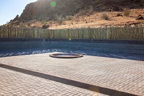 A paved area with a circular drain, a metal fence, and a hilly background. - At Kronenhof Lodge (Maltahohe)