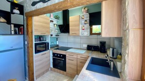 A compact kitchen with wooden cabinets, a built-in microwave, a stove, and a sink. - Le Petit Prince - Espace bien être avec Spa - Piscine chauffée (Sarlat-la-Canéda)