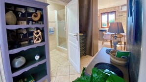 A hallway with a purple shelving unit, a glass shower, a wooden door, and a dining area with a table and chairs. - Le Petit Prince - Espace bien être avec Spa - Piscine chauffée (Sarlat-la-Can éda)