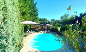 Ein Pool mit Liegestühlen und Sonnenschirmen, umgeben von viel Grün.