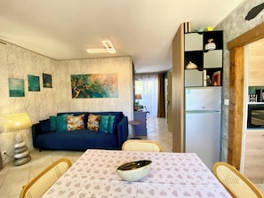 Ein Wohnzimmer mit einer Couch, einem Esstisch mit Stühlen, einem Kühlschrank und Kunstwerken an den Wänden.