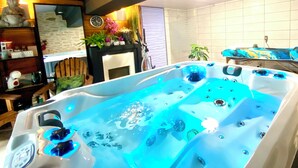 A hot tub with jets, a Buddha statue, a clock, and a potted plant. - Le Petit Prince - Espace bien être avec Spa - Piscine chauffée (Sarlat-la-Canéda)