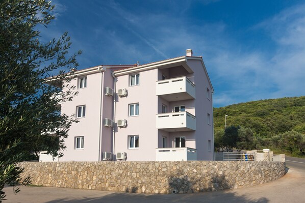 A multi-story building with balconies, air conditioning units, and a stone wall in front.