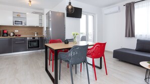 A modern kitchen with a dining area, a flat-screen TV, and a grey sofa.
