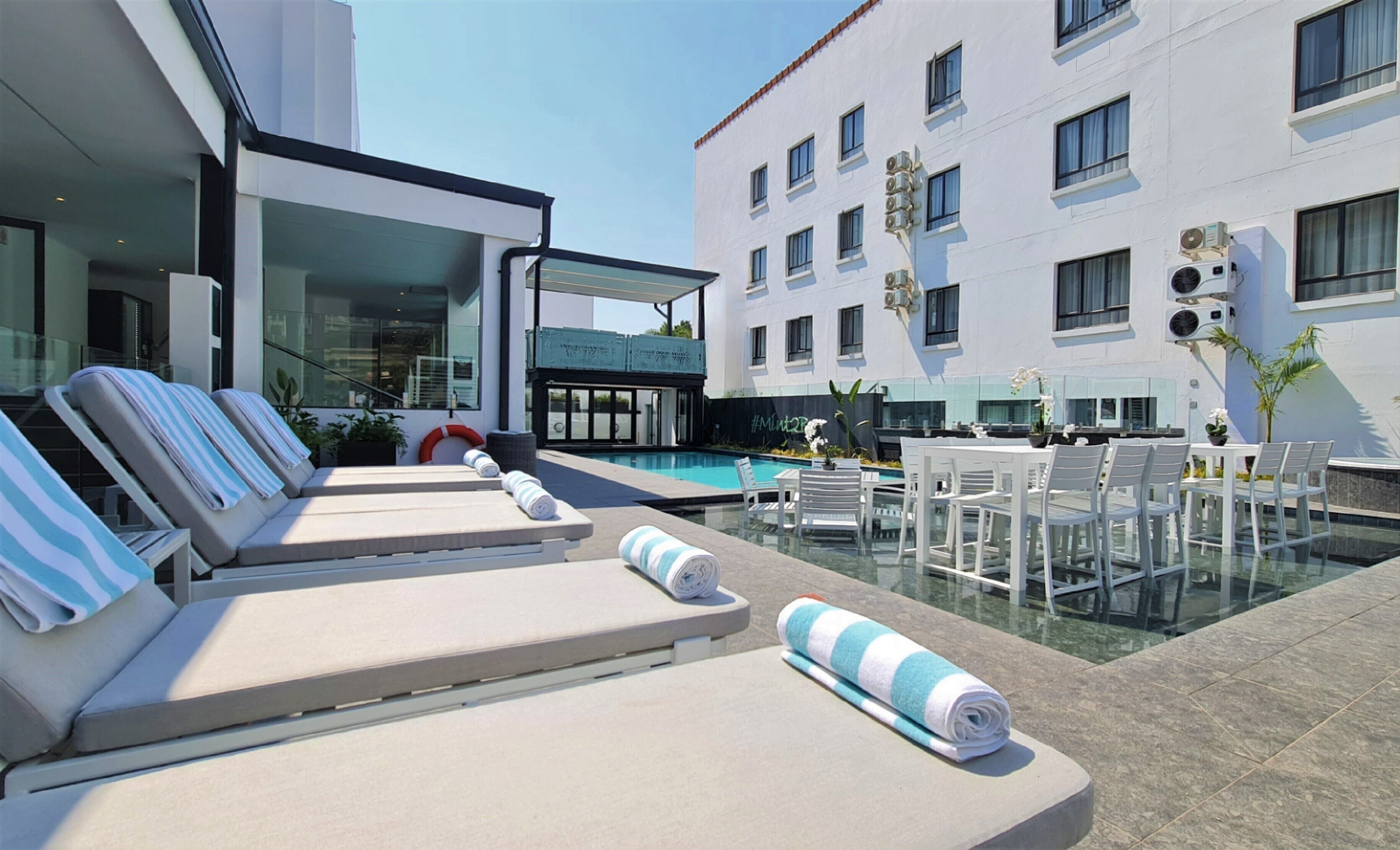 A poolside area with sun loungers, a glass table, and chairs.