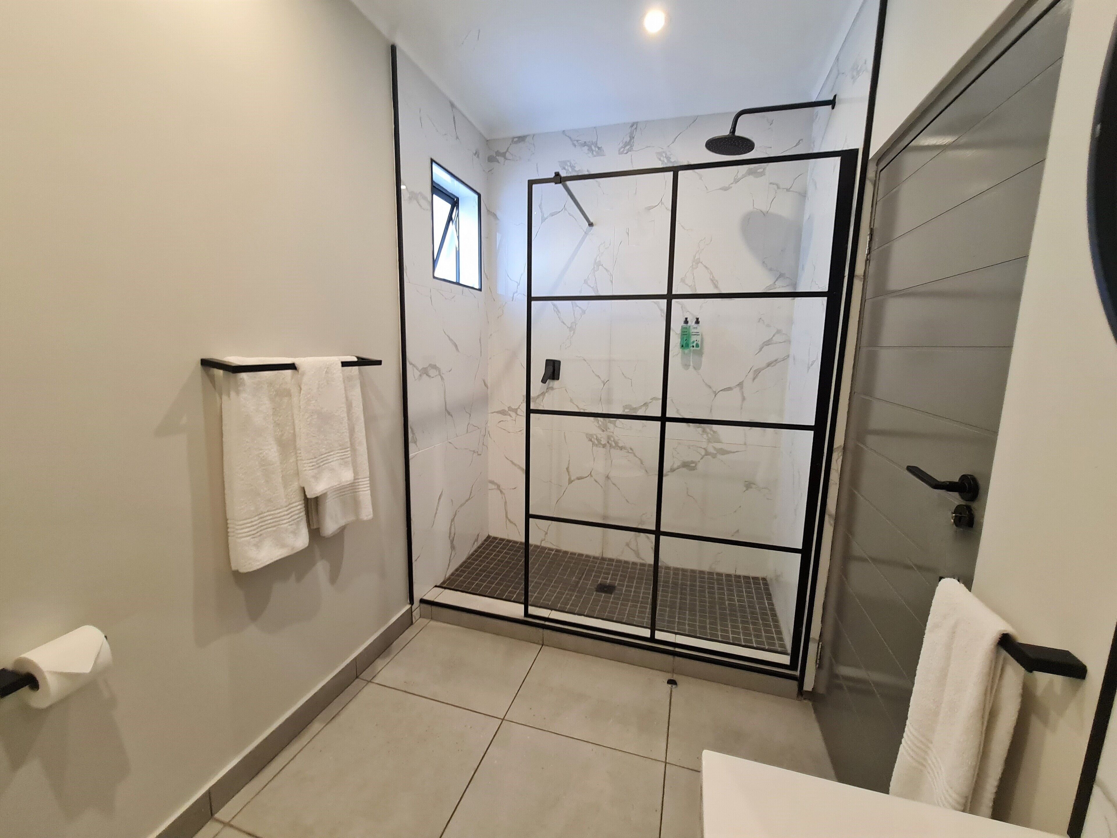 Un baño moderno con cabina de ducha de vidrio, un ventanal pequeño y un perchero para toallas.