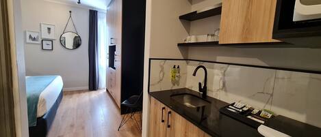 Une cuisine moderne avec des meubles en bois, un plan de travail noir et un évier. Dans la pièce adjacente, on trouve un lit recouvert d’une couverture bleue.