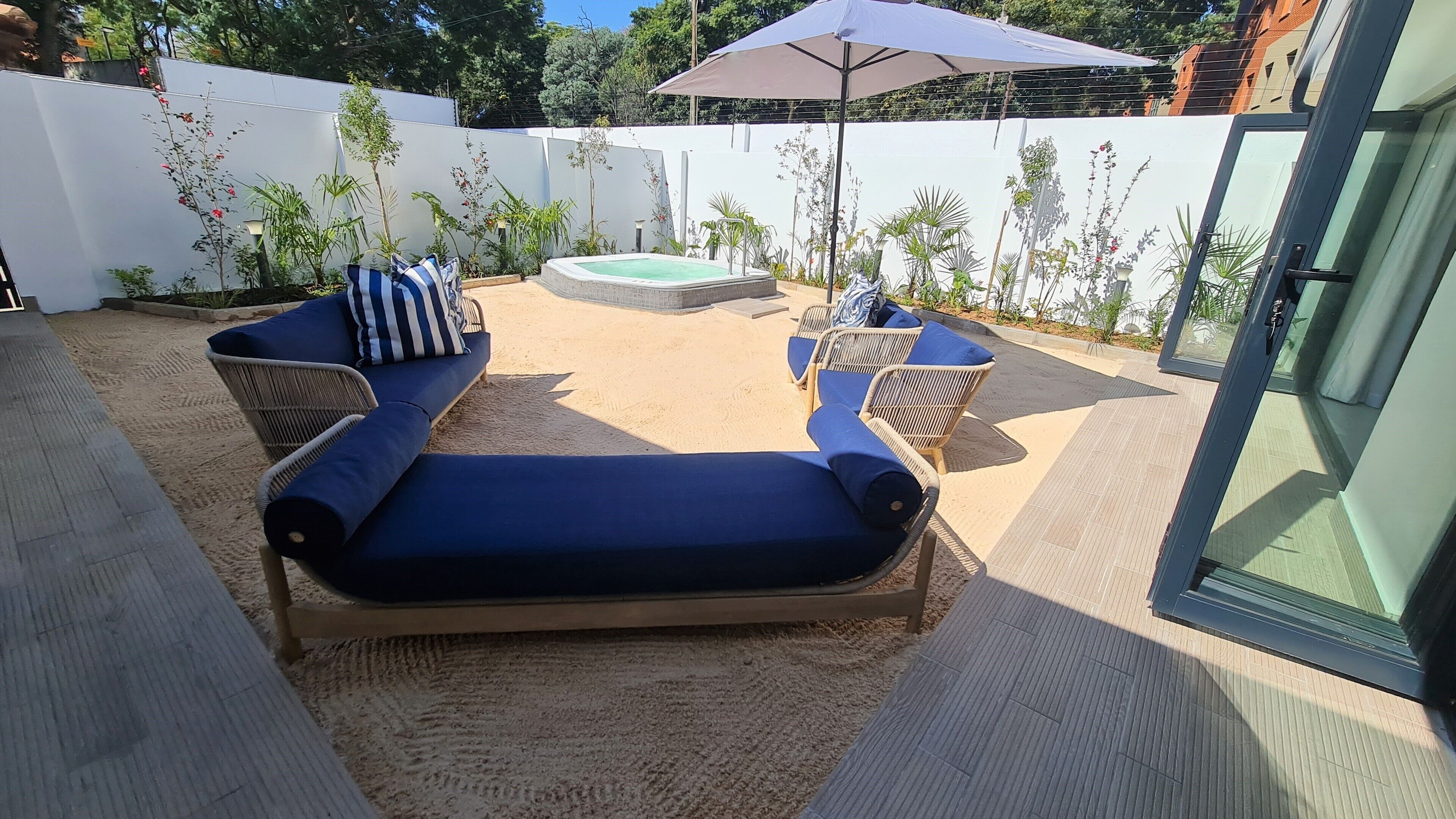 Eine sonnendurchflutete Terrasse mit einer blauen Couch, Korbstühlen und einem kleinen Whirlpool.