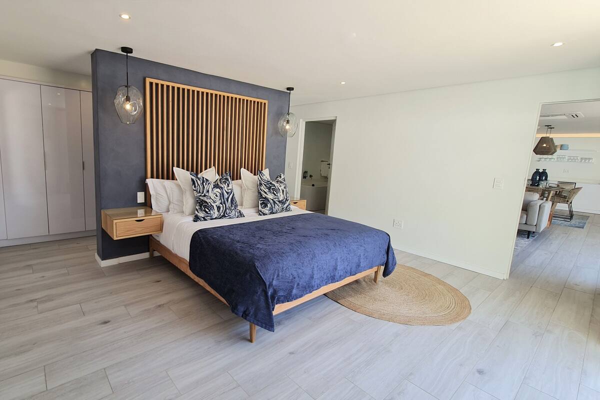 A modern bedroom with a bed, bedside tables, and a wall-mounted light fixture.