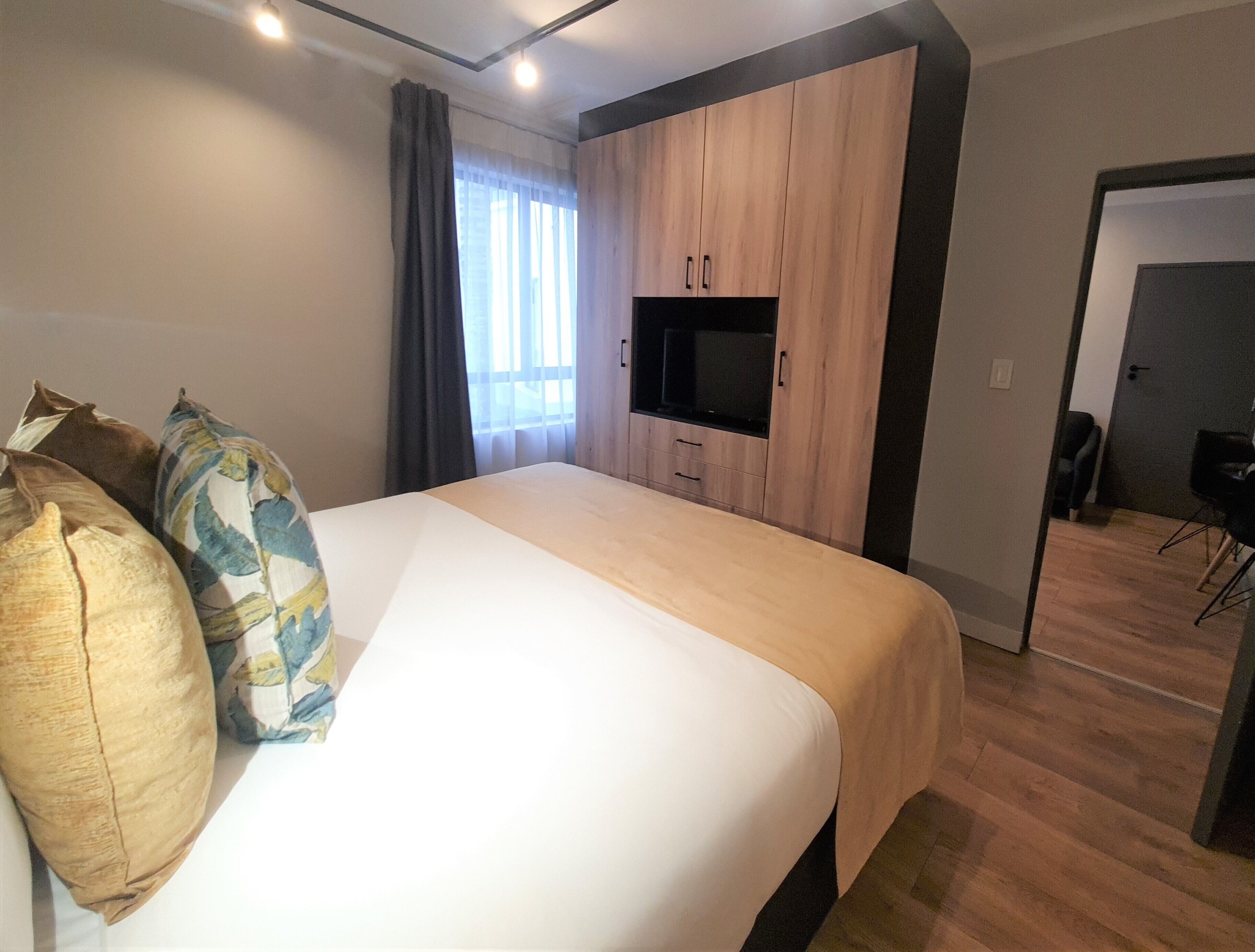 A hotel room with a bed, a TV, a wardrobe, and a desk.