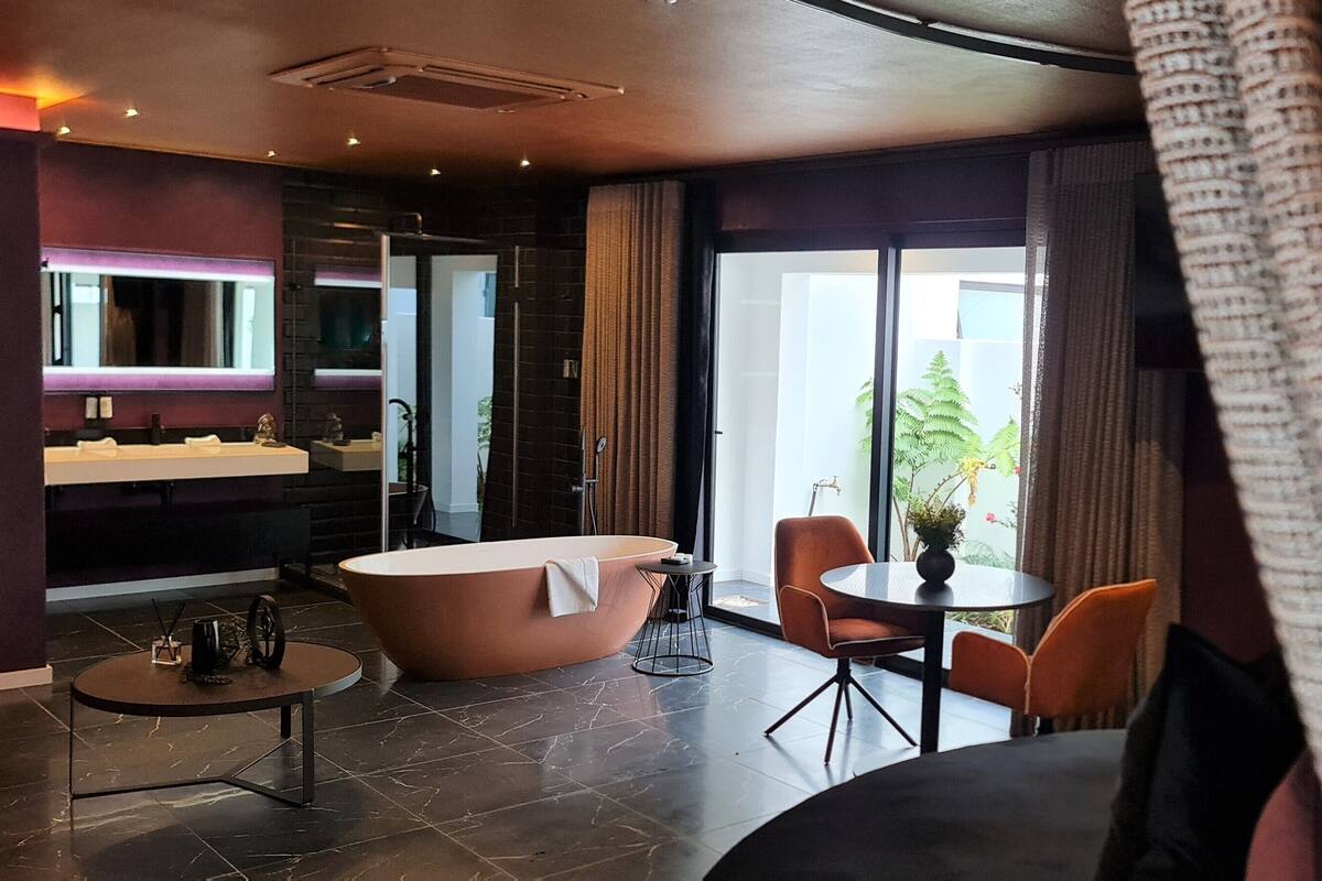 A modern bathroom with a freestanding bathtub, a vanity with a mirror, and a round table with chairs.