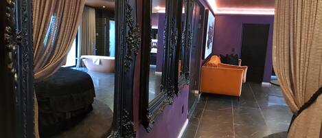 A hotel corridor with ornate black-framed mirrors, a purple wall, and a modern orange seating area.