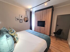 Un dormitorio moderno con una cama grande, un televisor montado en una pared de madera, una silla y una puerta.