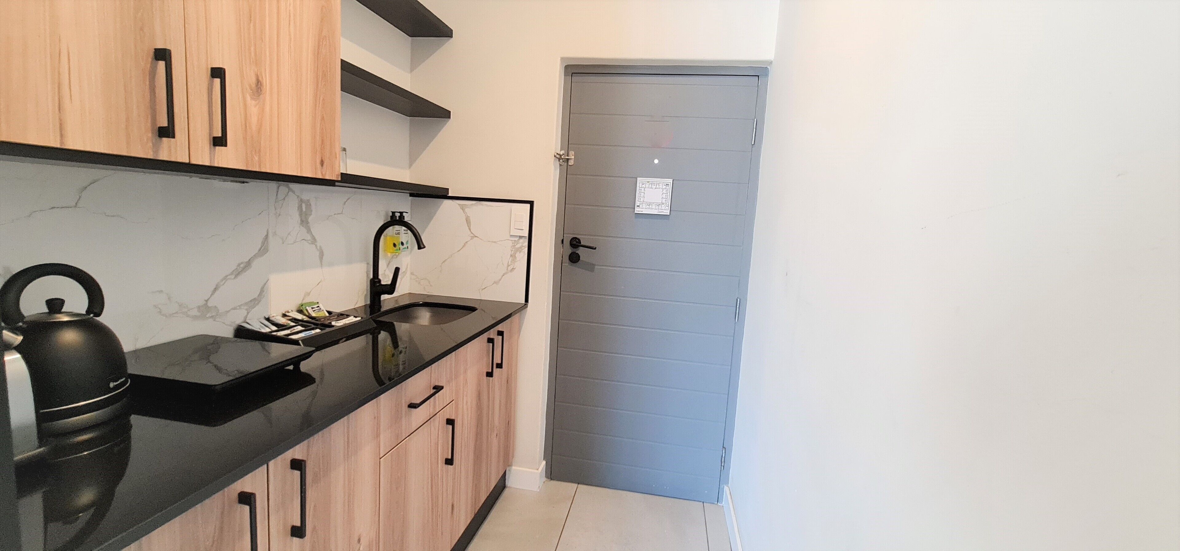 Una cocina con encimera negra, armarios de madera, una tetera y un lavabo.