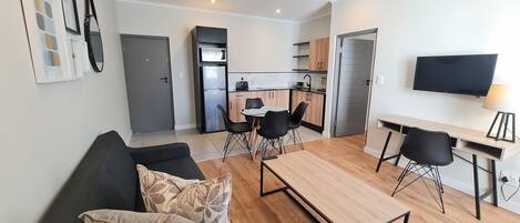 A modern apartment with a living room, dining area, kitchenette, and a TV.