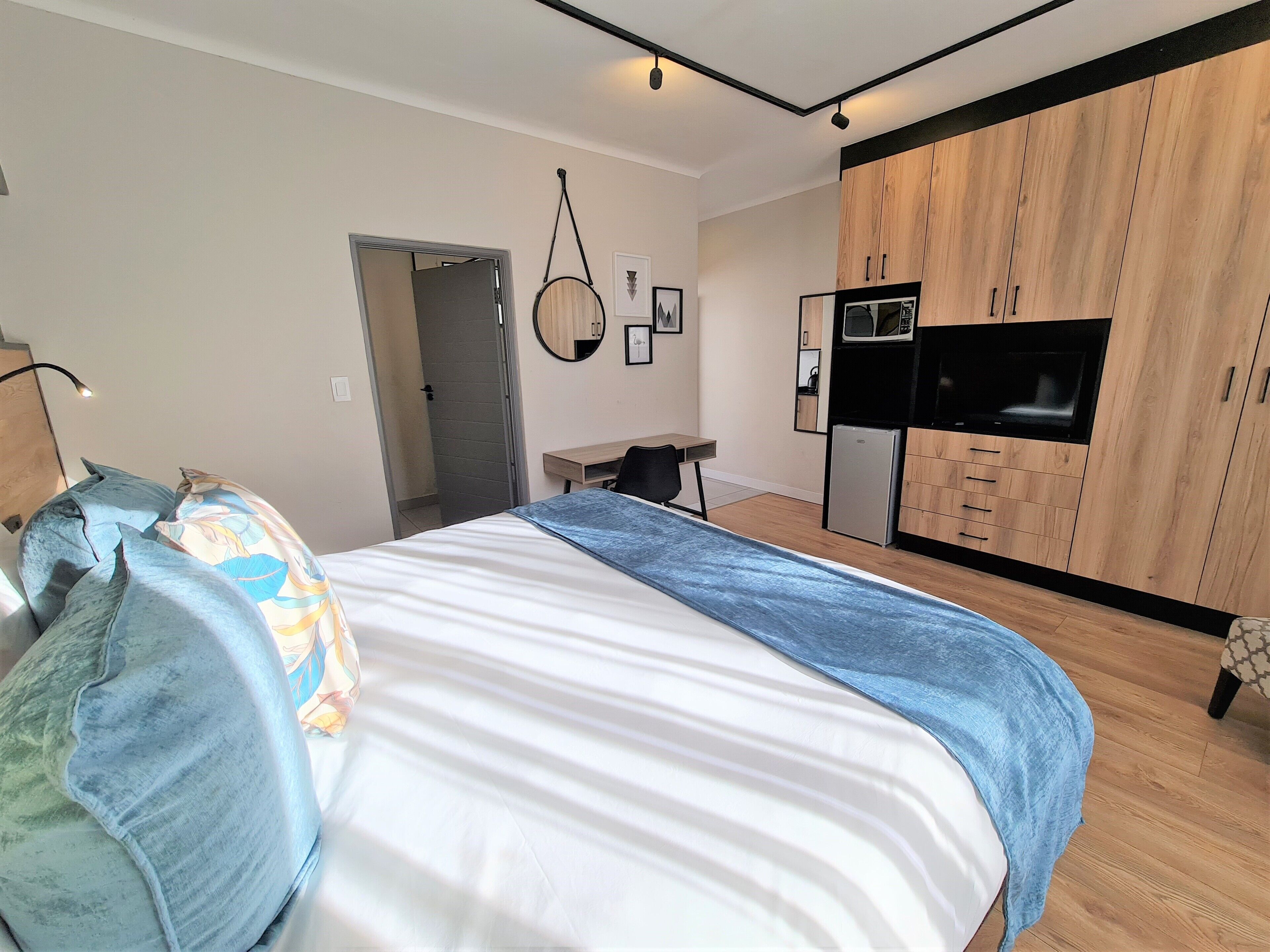 A modern bedroom with a bed, a desk, a kitchenette, and a TV.
