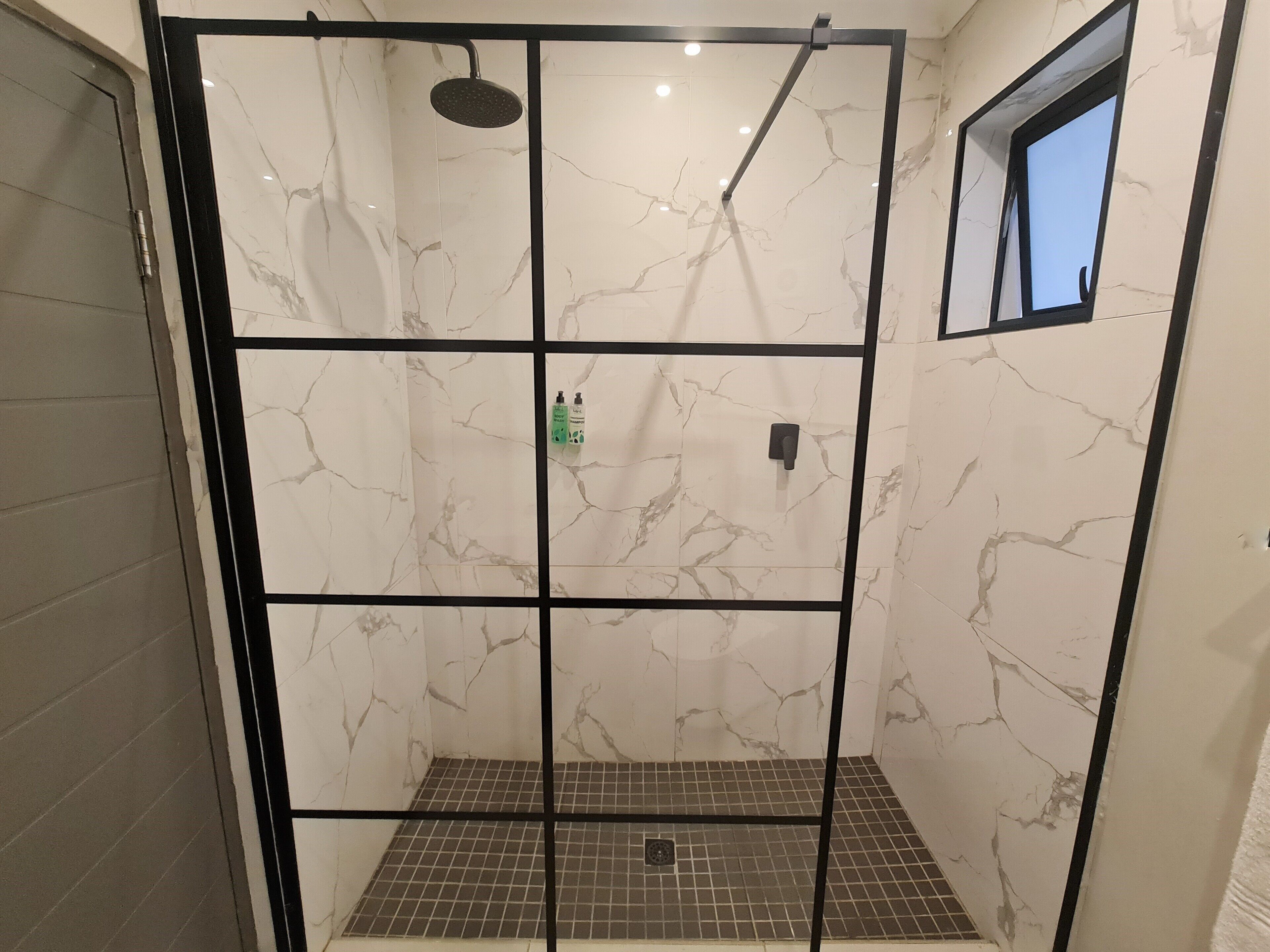 A walk-in shower with a grid floor, a handheld showerhead, and a small window.