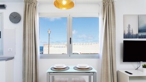 Una sala de estar moderna con un ventanal grande, un televisor de pantalla plana y una mesa de comedor con dos taburetes.