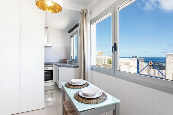 A modern kitchen with a dining area, large windows, and a view of the sea.
