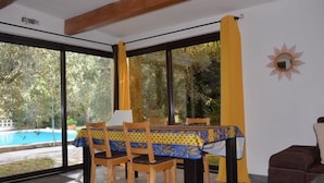 A dining area with a table set for four, large windows, and a view of a swimming pool. - Holiday home on a quiet, shady, private property (Arles)