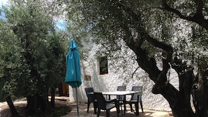 An outdoor patio with a table and chairs, surrounded by trees and a white wall. - Holiday home on a quiet, shady, private property (Arles)