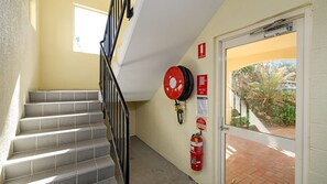 A staircase with a fire hose reel mounted on the wall, a fire extinguisher, and a door leading to an outdoor area.