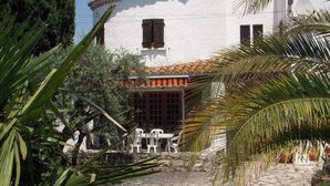 A white building with a tiled roof, a stone pathway, and a small patio area with chairs and tables. - Holiday flat of the size of 45 m² on a large estate with pool close to Arles (Arles)