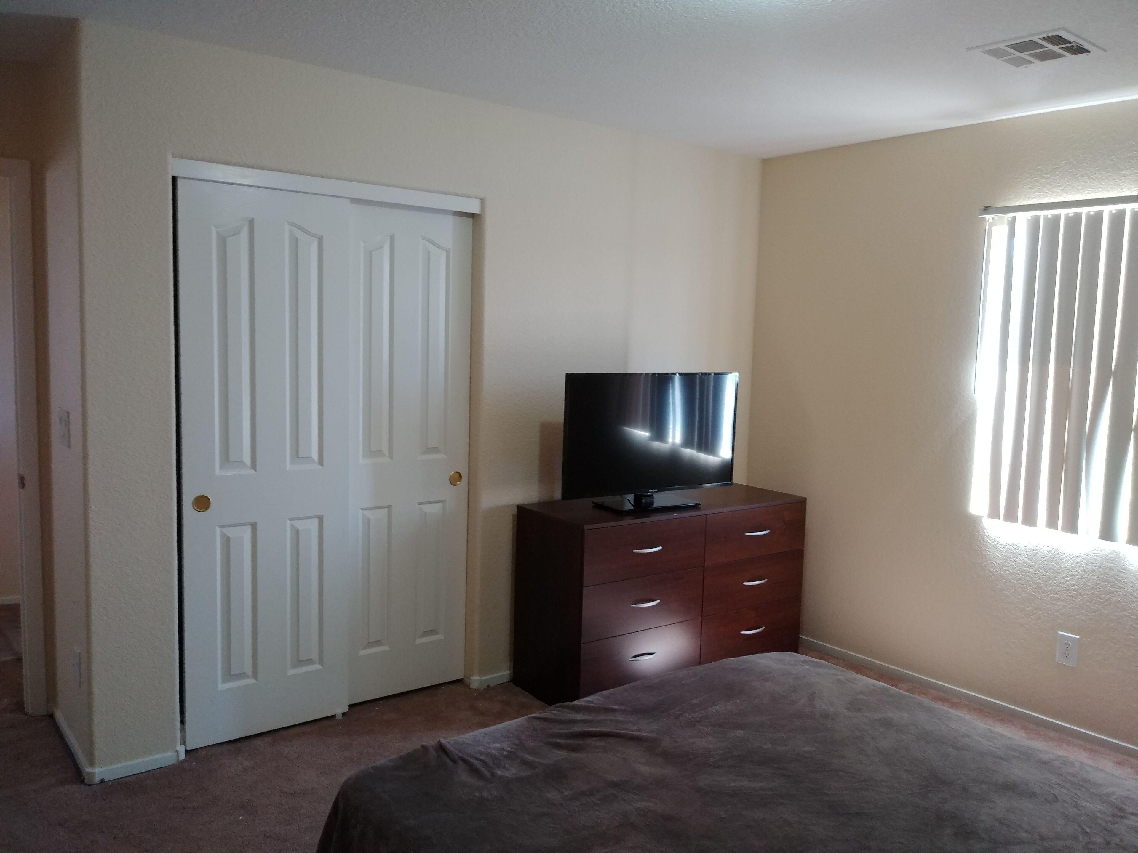 Ein Schlafzimmer mit Bett, Kommode, Fernseher und Tür.