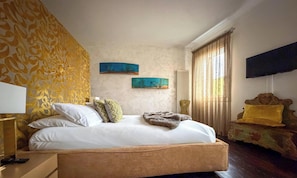 A bedroom with a bed, a nightstand, a TV, and two paintings on the wall. - MURANO Suites | COBALT (Venezia)