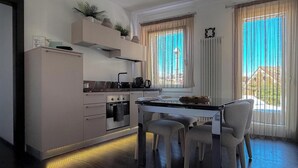 A modern kitchen with a dining area, built-in appliances, and a view through large windows. - MURANO Suites | COBALT (Venezia)