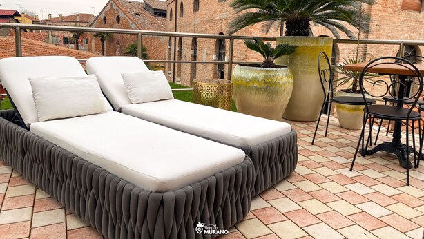 A rooftop terrace with two white lounge beds, a large potted plant, and a small table with chairs. - MURANO Suites | COBALT (Venezia)