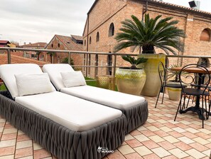 A rooftop terrace with two white lounge beds, a large potted plant, and a small table with chairs. - MURANO Suites | COBALT (Venezia)