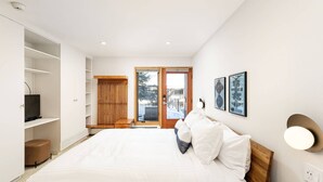 Une chambre moderne avec un grand lit, des étagères intégrées, une télévision et une porte-fenêtre coulissante donnant sur un balcon.