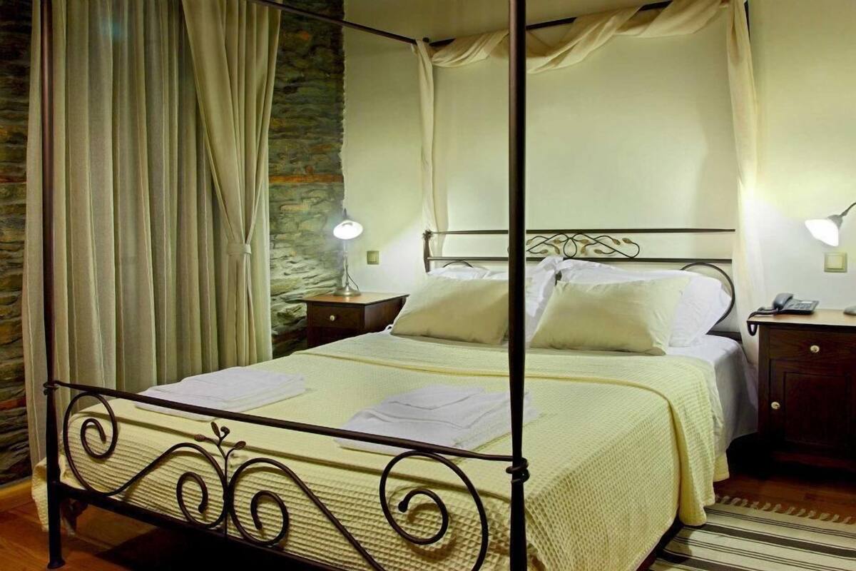 A four-poster bed with a canopy, a bedside table with a lamp, and a nightstand with a phone.