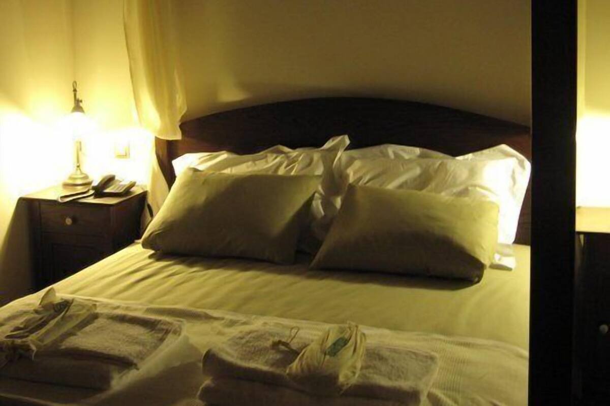A neatly made bed with pillows and folded towels, a bedside lamp, and a wooden headboard.