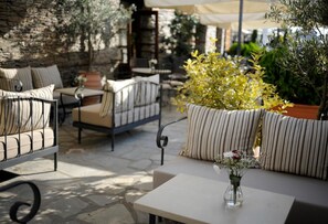 An outdoor seating area with cushioned chairs and a table, surrounded by potted plants and a stone wall. - Hotel Marelia (Polygyros)