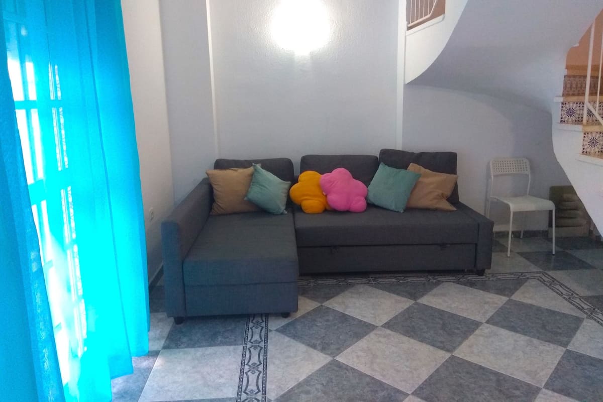 Ein Wohnzimmer mit grauem Sofa, gefliestem Boden und einer Treppe mit Musterfliesen.