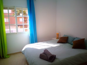 A bedroom with a bed, pillows, a nightstand, a lamp, and a window with curtains. - Enjoy Málaga La Cala (Rincon de la Victoria)