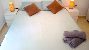 A neatly made bed with white bedding, two brown pillows, and two nightstands with lamps.